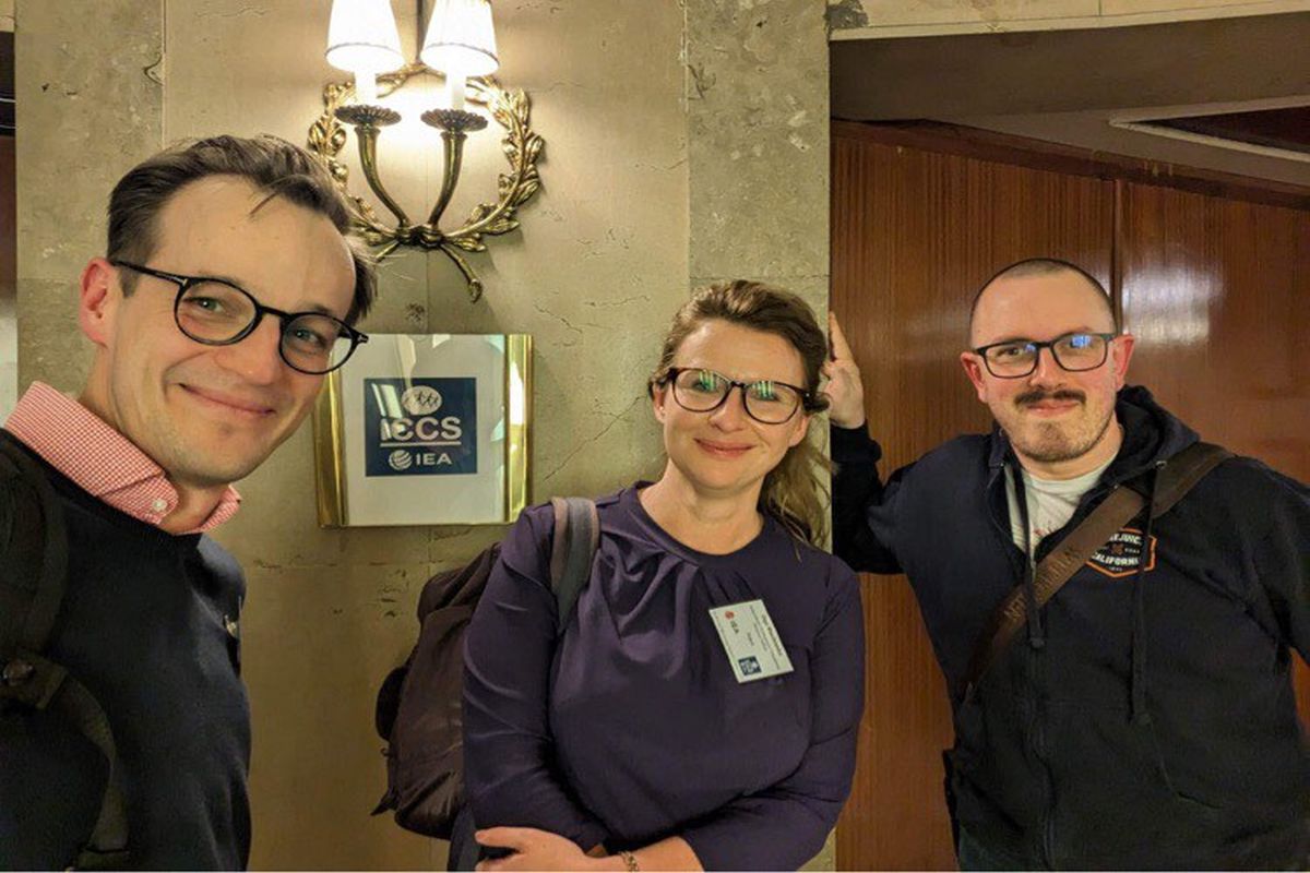 Trójka uśmiechniętych uczestników z polskiego zespołu realizatorskiego na tle loga ICCS.